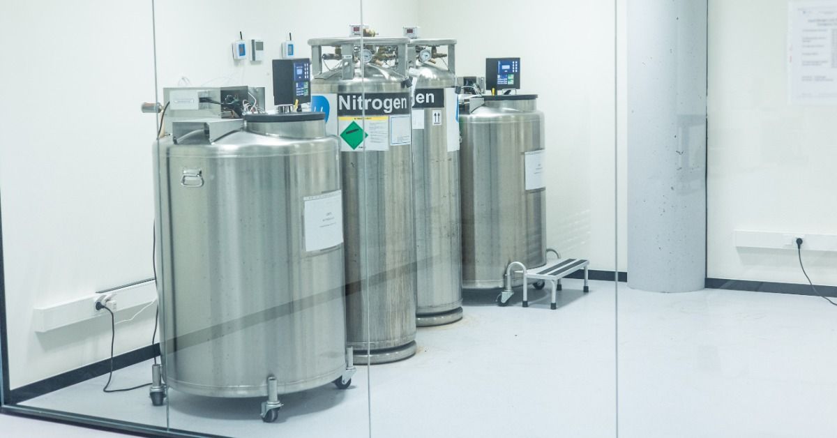 Stainless steel nitrogen storage vessels stand inside a clean industrial facility behind glass.