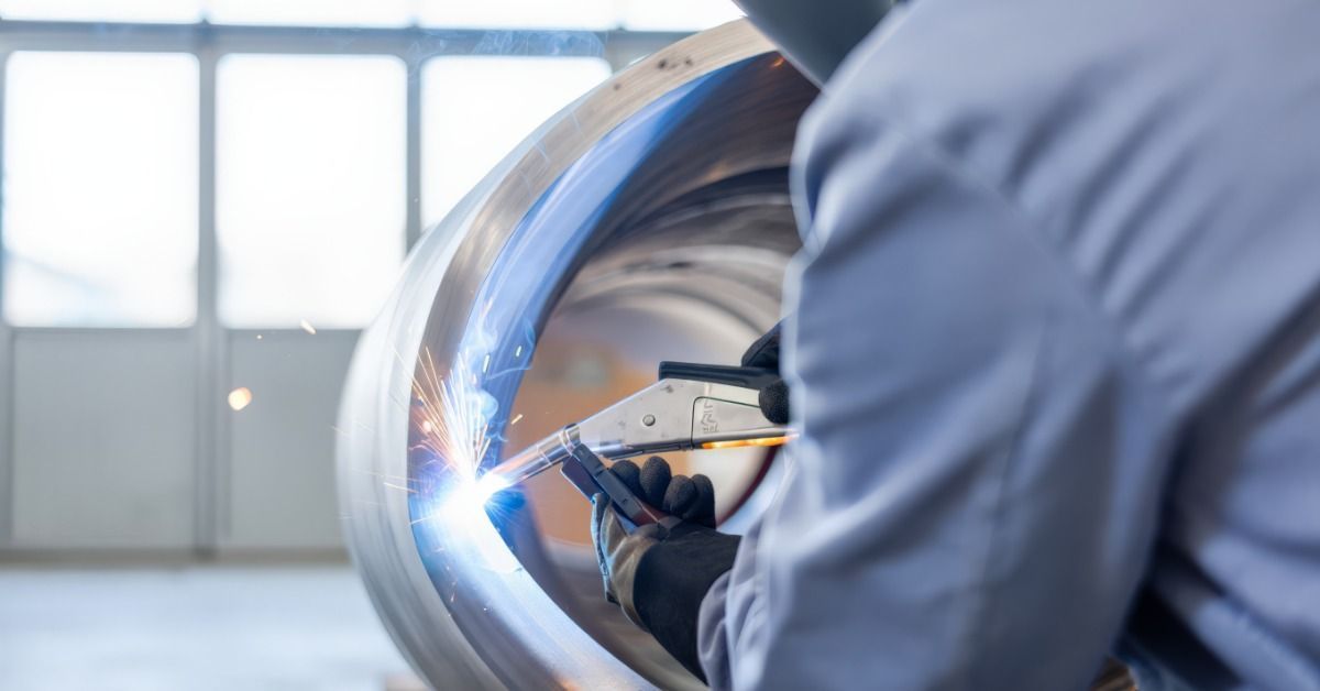 A worker welds the curved interior of a large stainless steel vessel during industrial fabrication work.
