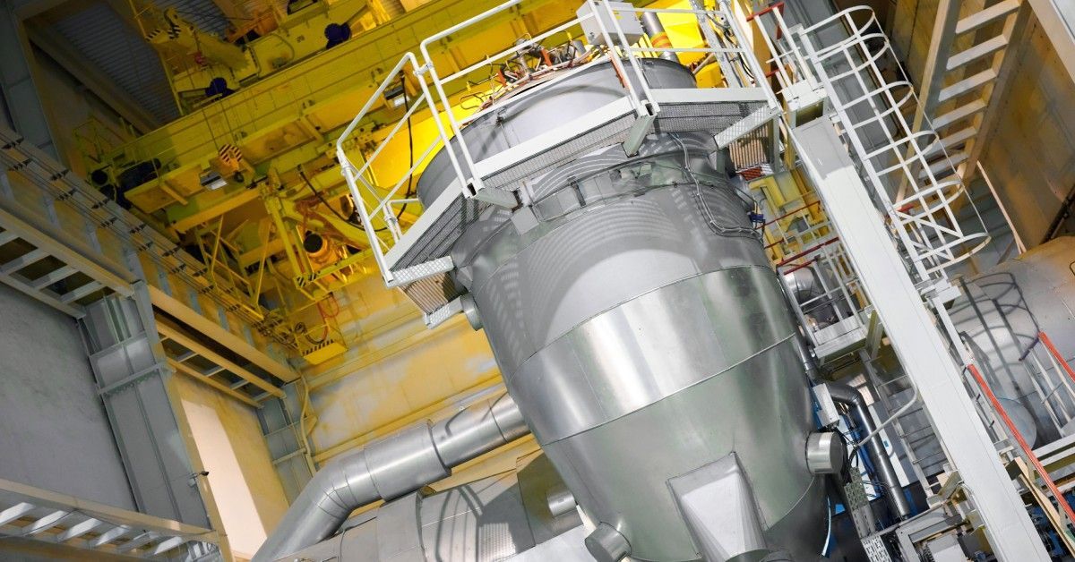 A large stainless steel industrial duct system features access stairs on the side and a platform running along the top.