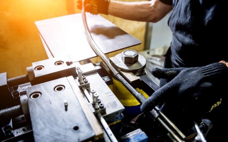 A worker bends a metal pipe with an industrial machine, shaping tubing precisely for fabrication.