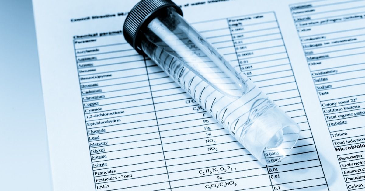 A drinking water sample rests on chemical test results used to evaluate water quality and chemical conditions.