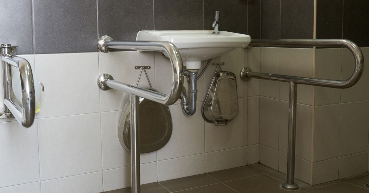 Stainless steel safety rails surround a sink and connect to the tiled floor and walls at multiple mounting points.