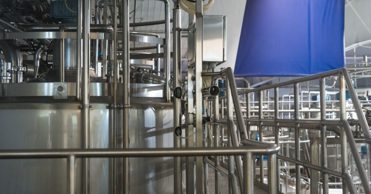 Stainless steel railings surround processing equipment and elevated walkways inside a large industrial facility.
