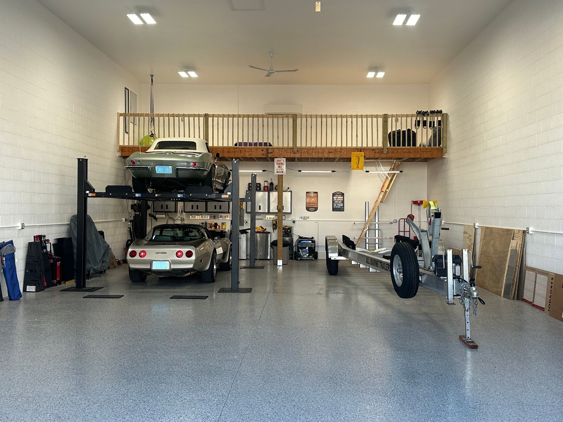 Spacious garage with car lift, parked vehicles, tools, and a loft storage shelf