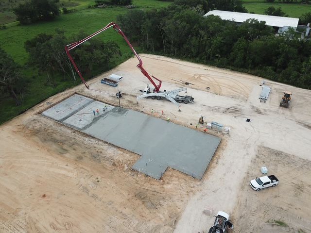 Aerial view of a construction site with a red concrete pump and a large concrete slab being poured.