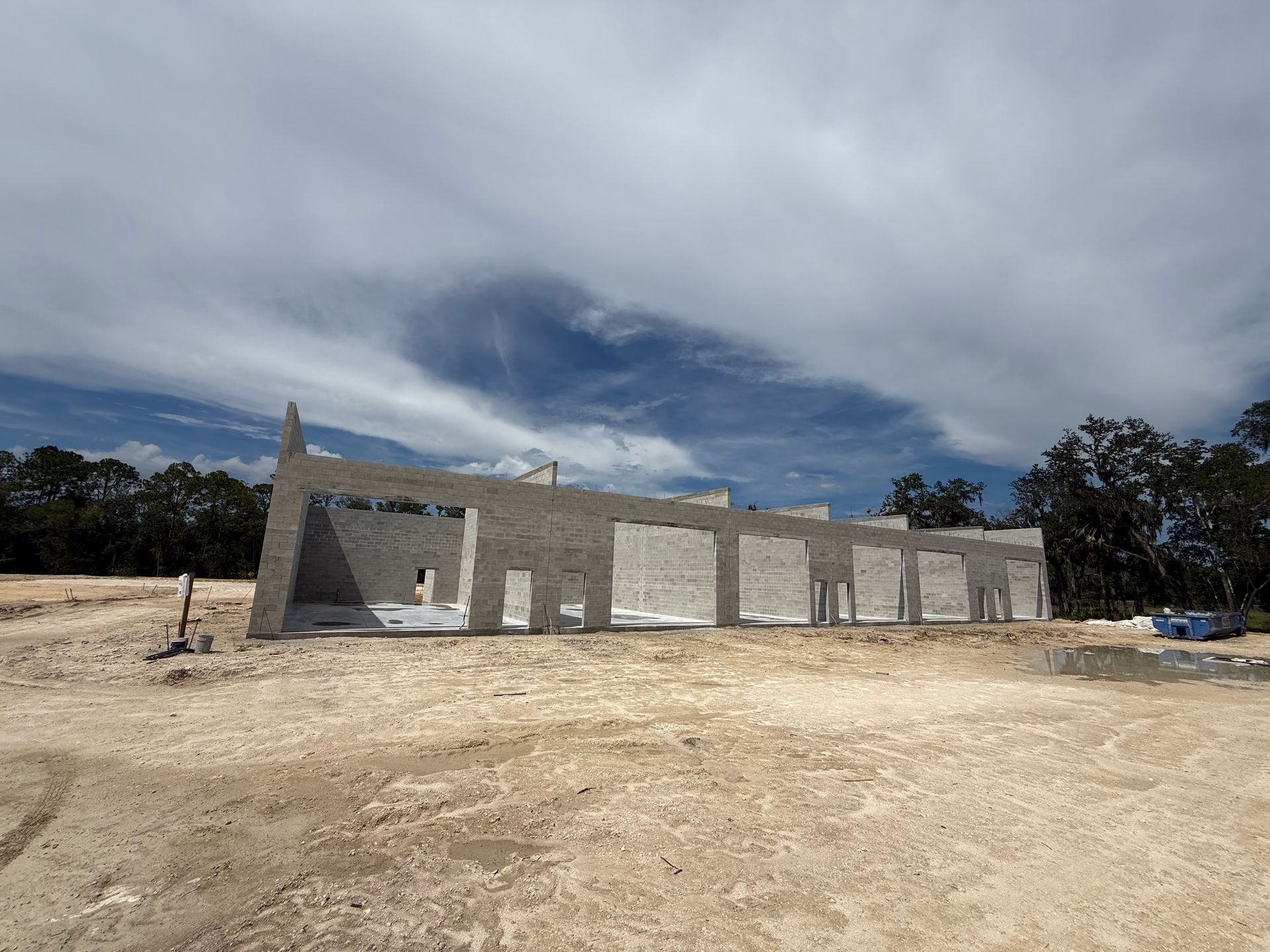 Partially built concrete building on a dirt lot under a cloudy sky