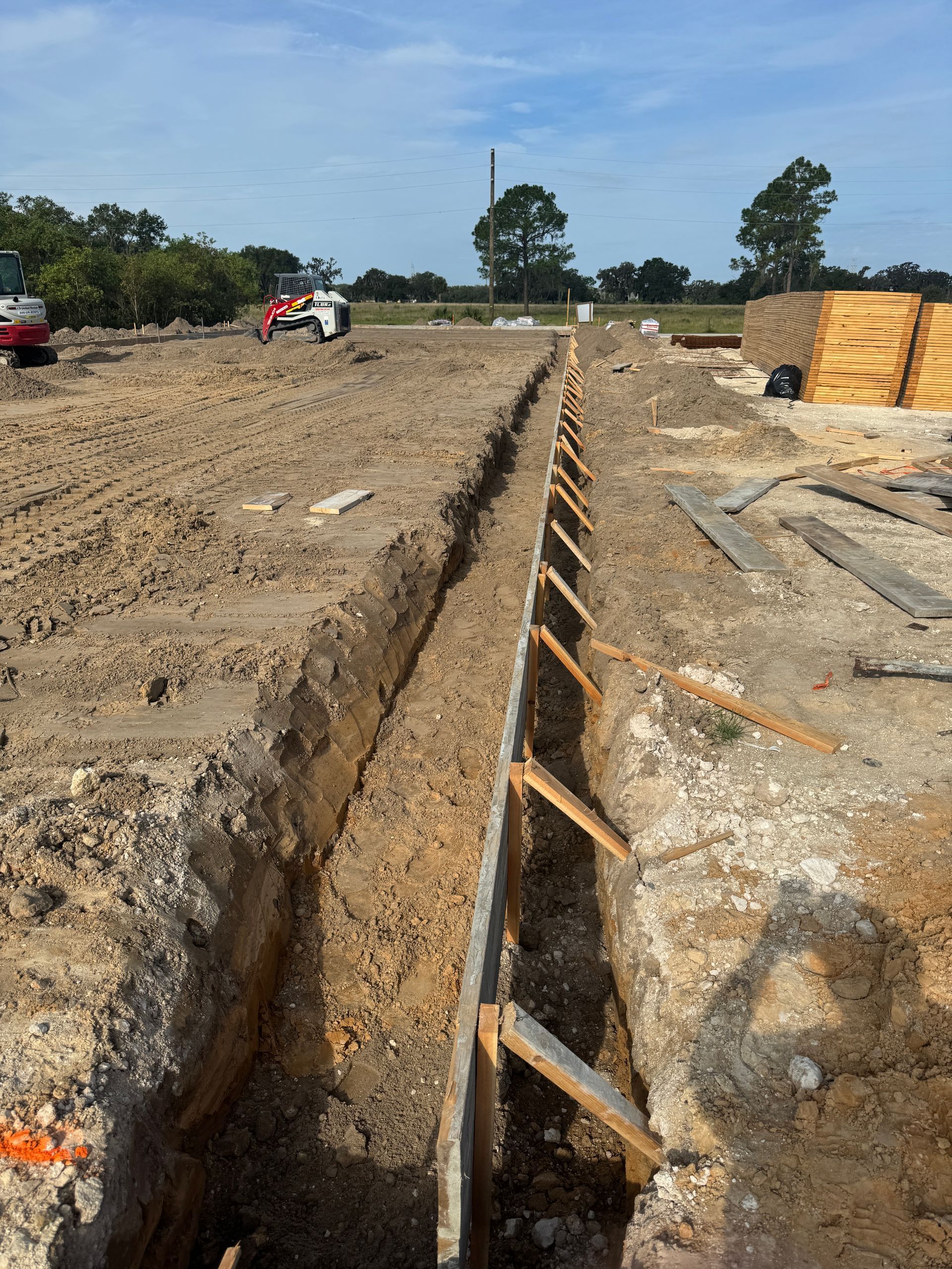Long trench with wooden supports at a construction site on a dirt field