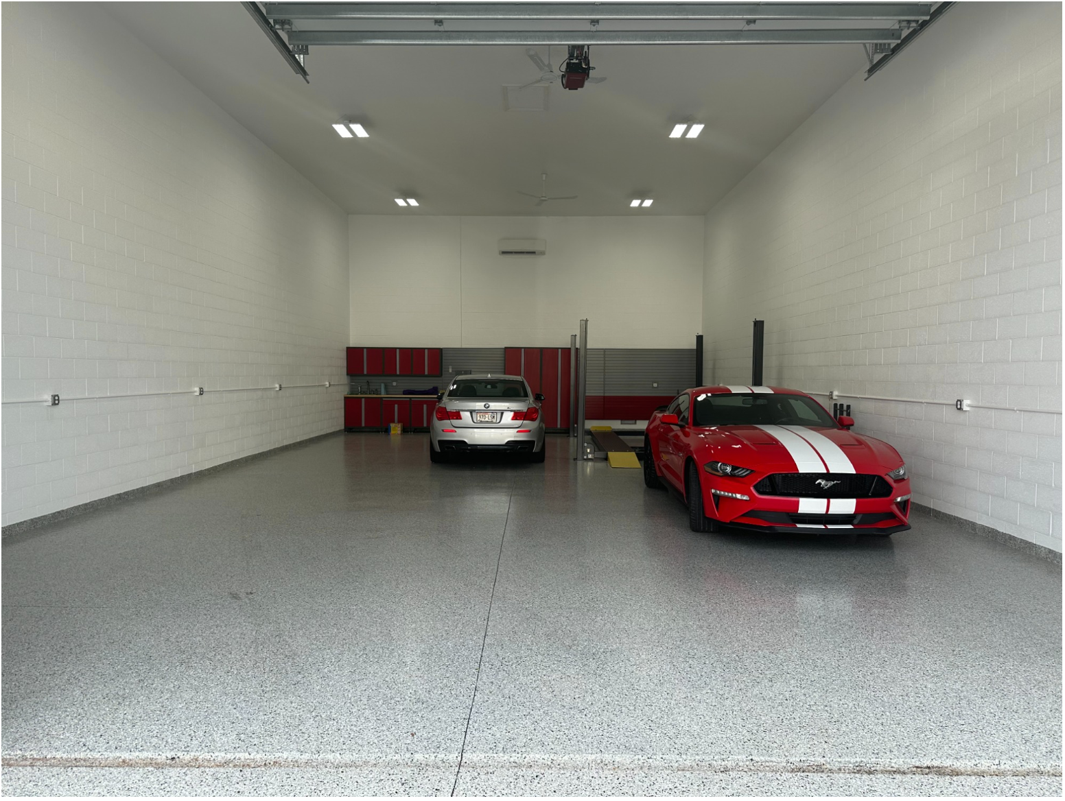 Two sports cars parked in a bright garage, one red with white stripes in front and one silver in back