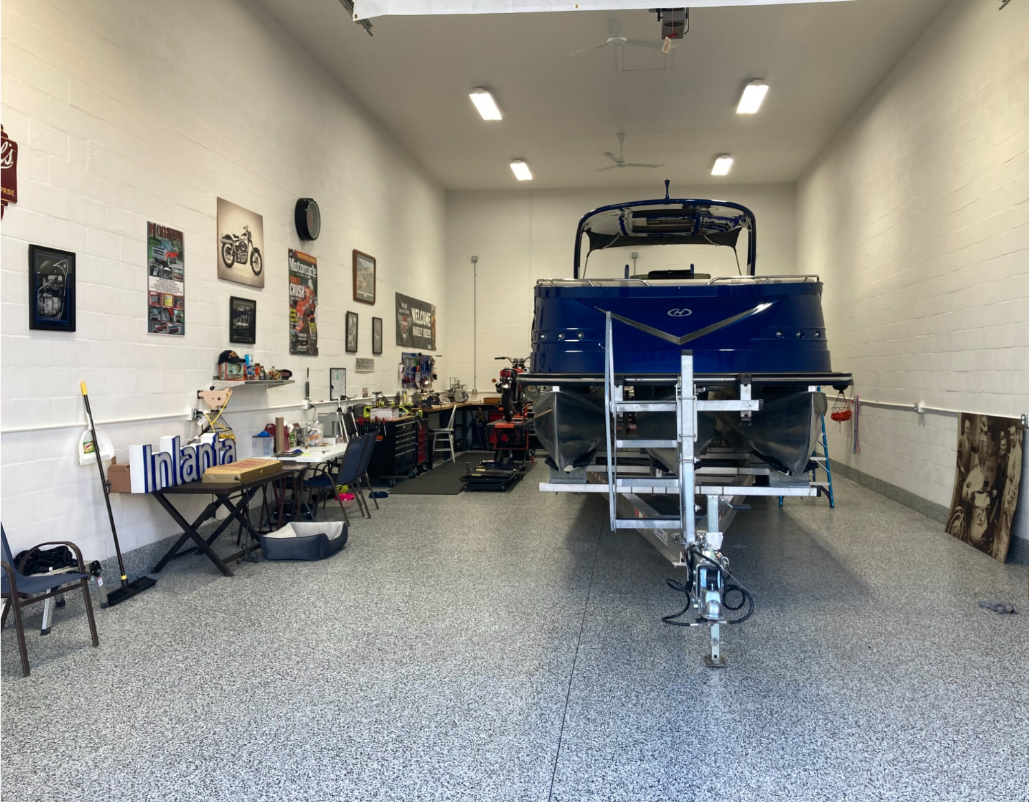 Boat storage garage with a blue boat on a trailer, tools, wall art, and a speckled floor