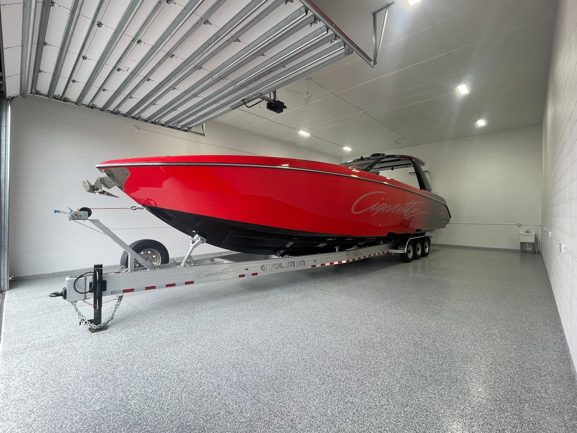Red speedboat on a trailer inside a garage with a speckled floor and open overhead door