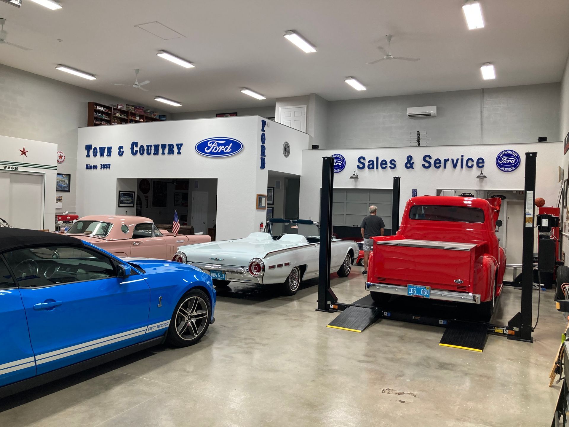 Auto service shop with several sports cars, including a blue car, white car, and red truck under repair.