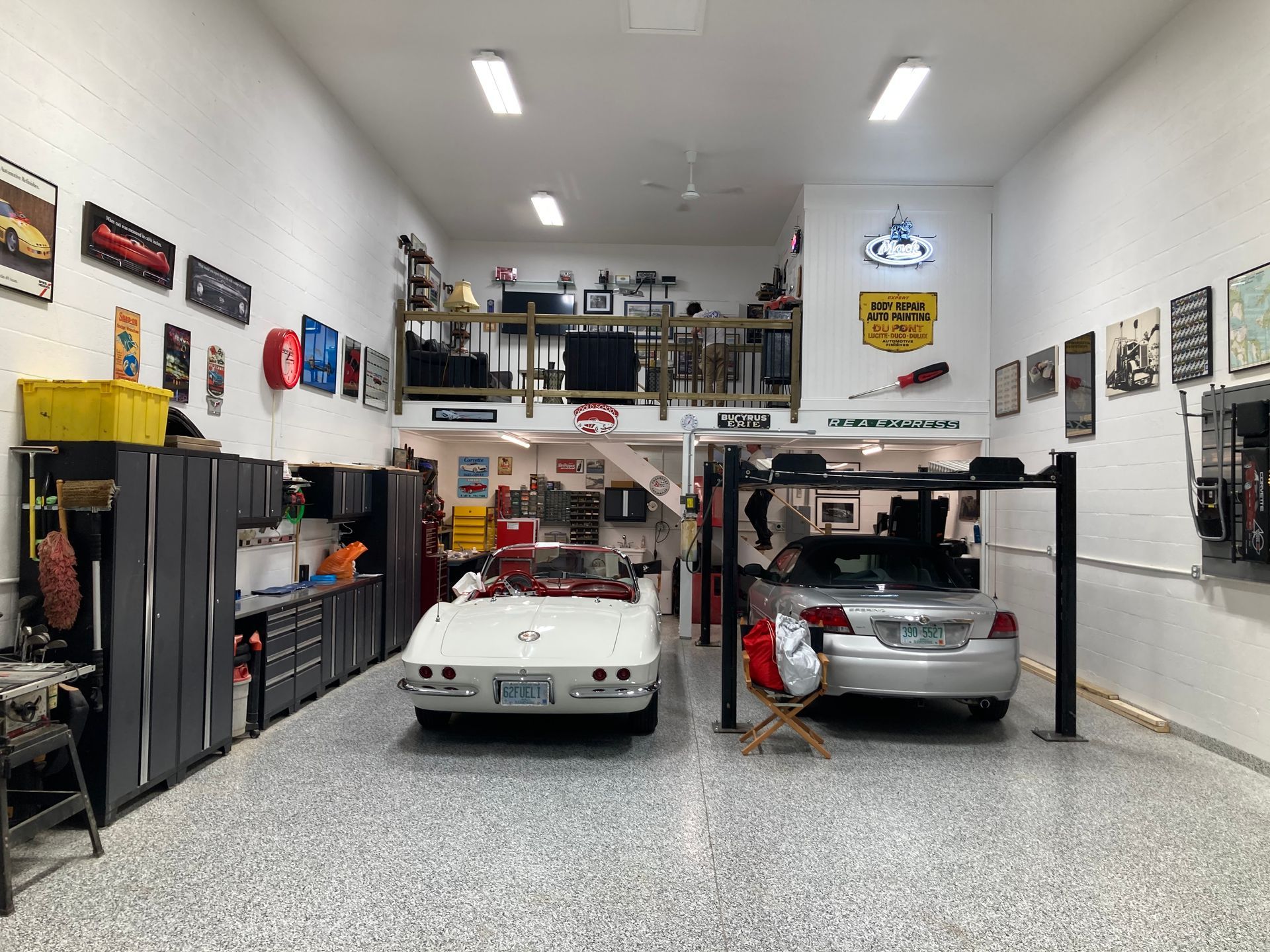 Car garage with two cars, tool cabinets, and a loft office under bright ceiling lights