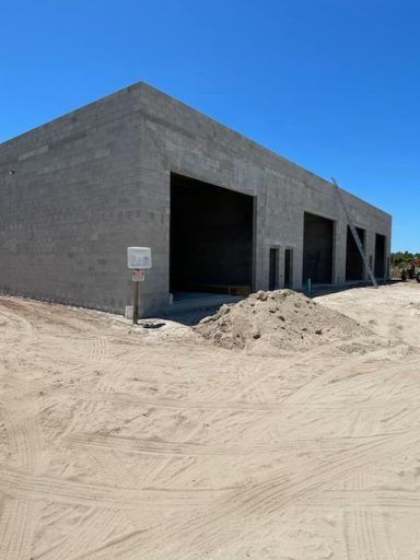 Unfinished concrete building under construction on a sandy lot under a clear blue sky