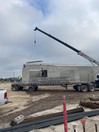Crane lifting a concrete structure on a construction site under a cloudy sky.