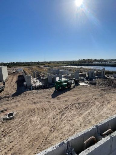 Construction site with green machinery and dirt roads under a bright blue sky near water