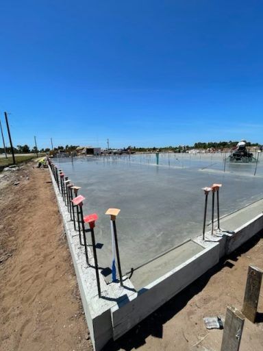 Concrete foundation slab at a construction site, with rebar stakes and wooden markers under a clear blue sky