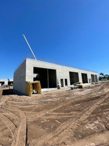 Unfinished concrete building under construction on a dirt lot under a clear blue sky
