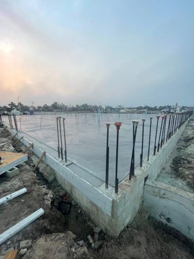 Reinforced concrete foundation slab under construction with exposed rebar at a site near water at sunset