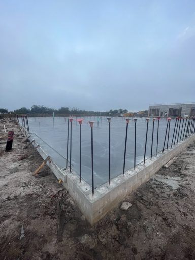 Construction foundation slab with exposed rebar at a muddy site under a cloudy sky