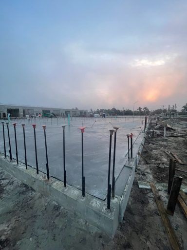 Concrete foundation under construction with exposed rebar beside a muddy site at dusk