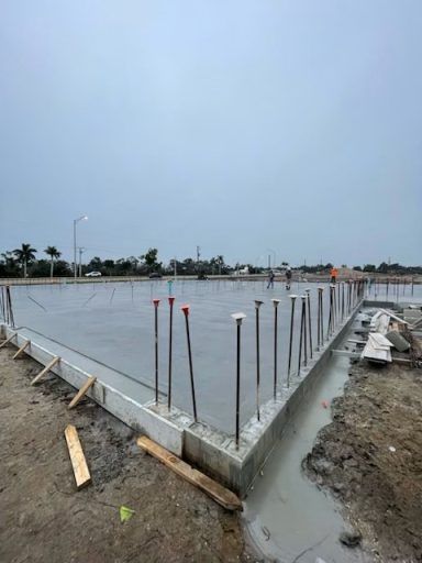 Freshly poured concrete foundation slab with exposed rebar on a muddy construction site outdoors