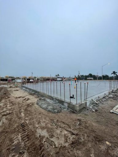 Construction site with concrete foundation slab and vertical rebar on muddy ground under overcast sky