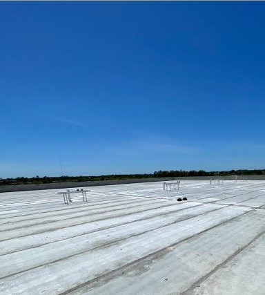 Flat white rooftop under a clear blue sky, with a few small roof fixtures in the distance.