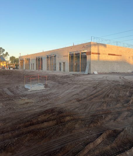 Construction site with a long concrete building in early evening light and a dirt foreground