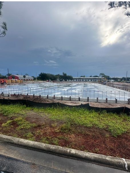 Rainy outdoor construction site with a large flooded or covered basin under a cloudy sky