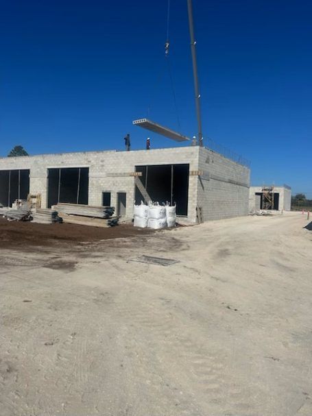 Construction site with a small concrete building, open doorways, and materials stacked outside under a clear blue sky