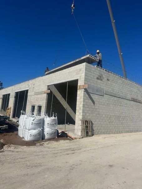 Construction site with a cinderblock building under a clear blue sky and workers on the roof.