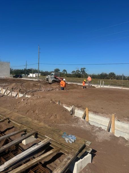 Construction workers in orange vests leveling dirt on a building site under a clear blue sky