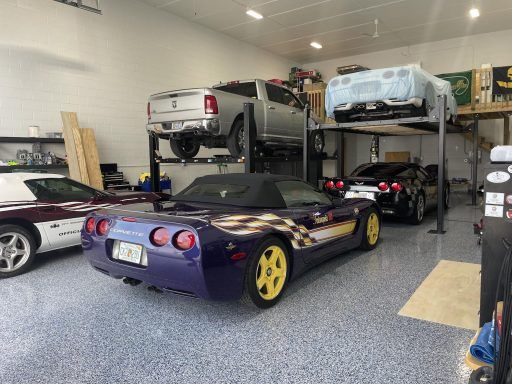 Two sports cars parked in a garage, including a purple convertible with yellow wheels.