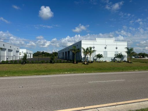 White industrial buildings beside a road under a blue sky with scattered clouds.