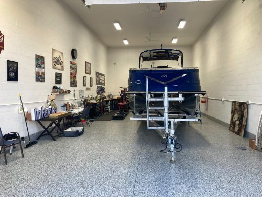 Blue boat in a garage-like workshop with tools, wall art, and a trailer hitch in the center.