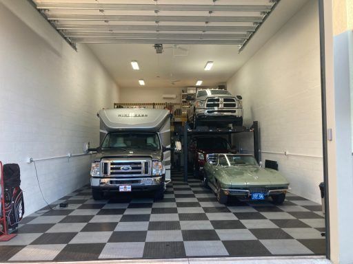 Indoor garage with checkered floor, a white truck, a blue car, and a car lift with stacked vehicles.