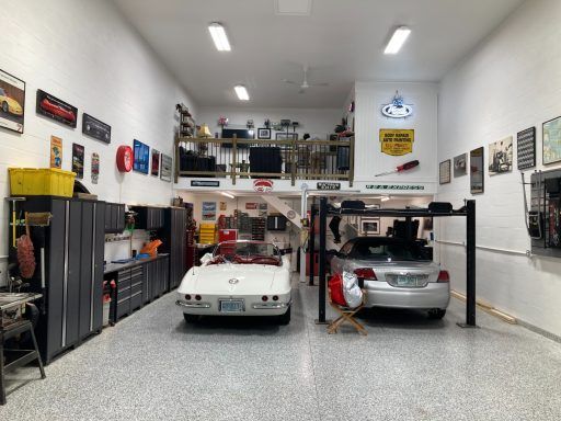 Two cars parked in a bright garage with shelves, tools, and wall signs
