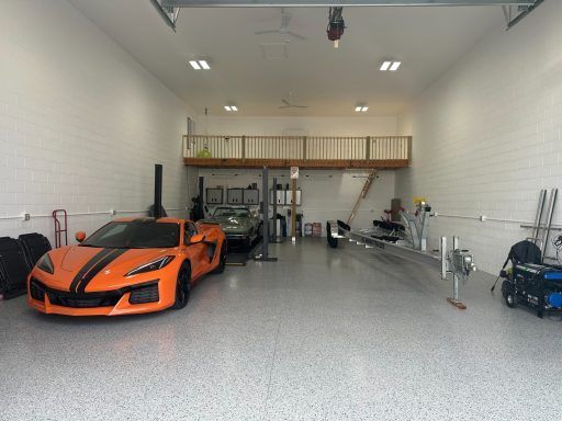 Orange sports car in a bright garage with tools, shelving, and a mezzanine loft