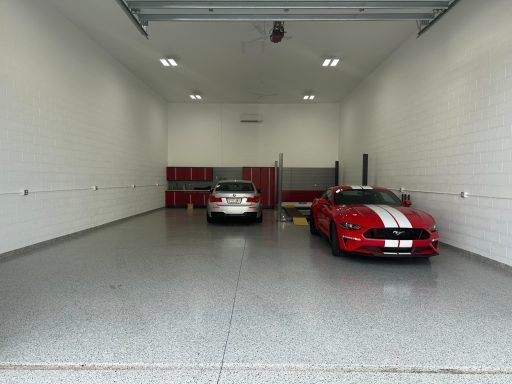 Two sports cars parked inside a bright, empty garage, one red and one silver.
