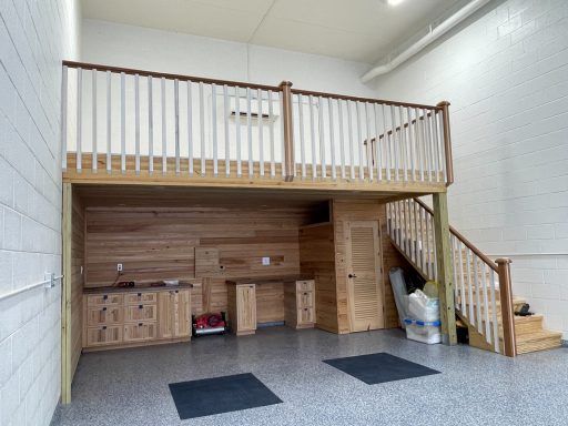 Lofted storage area with wooden cabinets, stairs, and railing in a bright utility room