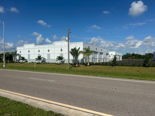 White industrial building beside a road under a blue sky with scattered clouds.