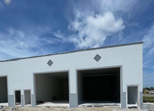 White stucco building with two open garage bays under a partly cloudy blue sky