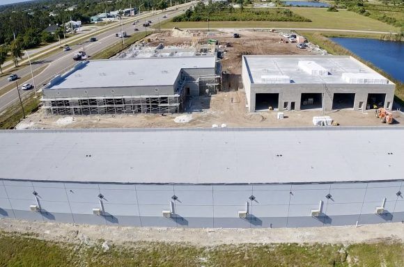 Aerial view of an industrial building site with two large gray buildings beside a roadway and grassy fields.