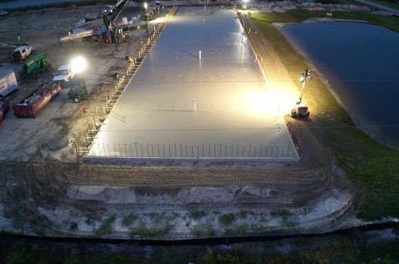 Nighttime construction site with large, brightly lit concrete slab being worked on by heavy machinery