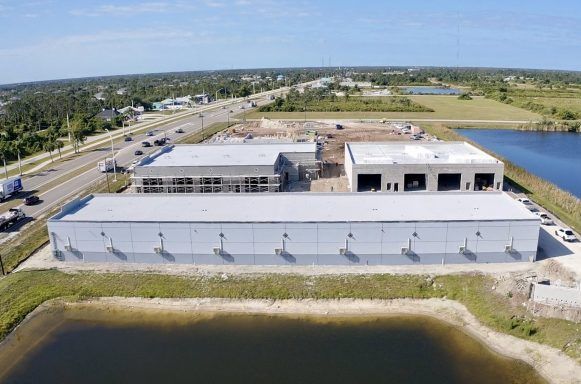 Aerial view of an industrial building complex beside water, with roads and open land nearby.