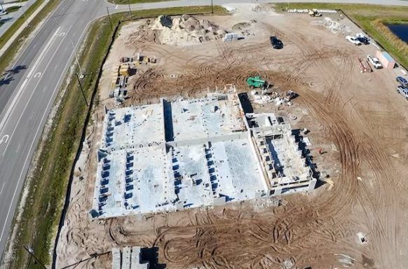 Aerial view of a large building under construction beside a road on a dirt lot