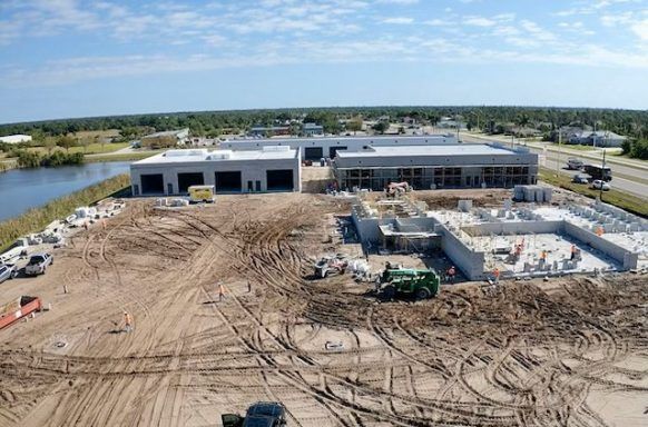 Aerial view of a large construction site with a new building, dirt lot, and heavy equipment.