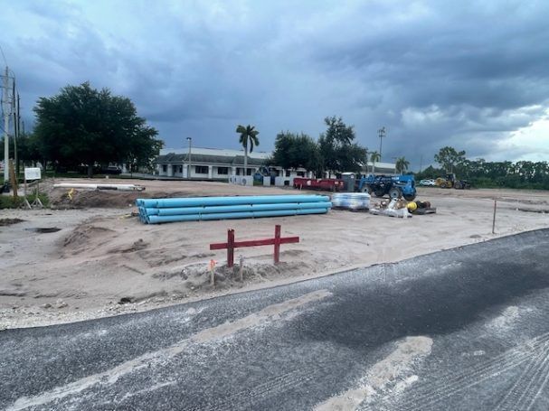Construction site with blue pipes, a red barrier, and cloudy sky beside a road
