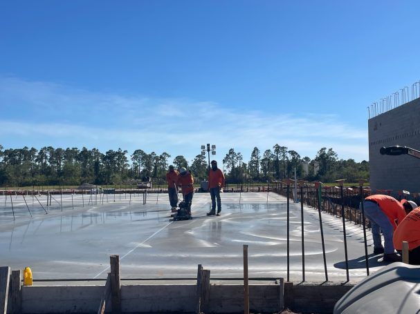 Workers in red shirts on a concrete construction slab under a clear blue sky