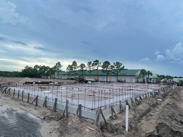 Construction site with concrete foundation footings, rebar, and formwork under a cloudy sky